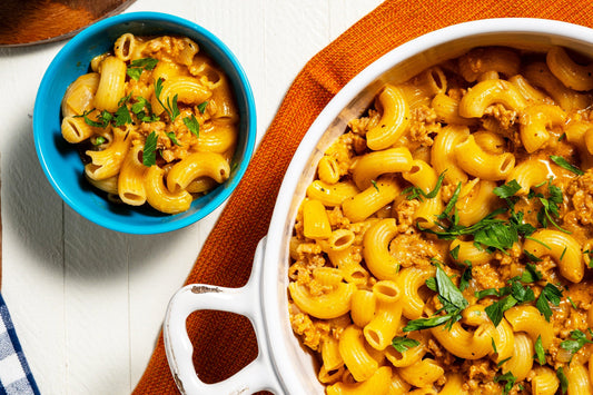 A skillet full of Cheesy Turkey Pasta sits next to a small bowl with one serving or pasta.