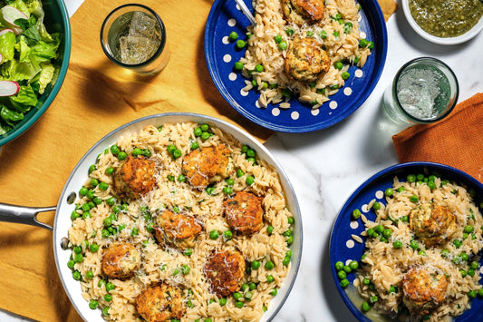 A skillet and two plates filled with One Pan Orzo with Chicken Meatballs, Peas & Pesto.