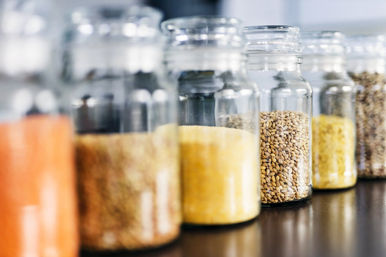 Row of glass jars with various seeds and grains on a wooden surface