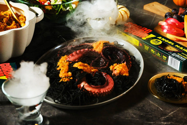 Garnished dish with black squid ink pasta, octopus, and vegetables on a dark surface with smoke effect.