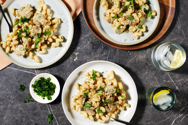 Plates of pasta with meat and greens on a dark surface with side dishes.