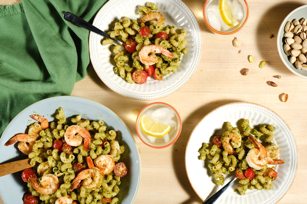 Pasta with shrimp and vegetables on a wooden table with lemon slices and a green towel.