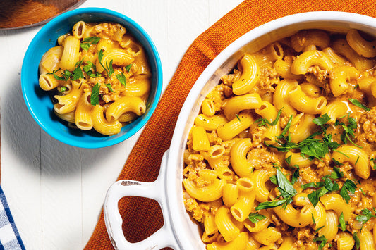 Two bowls of macaroni and cheese with ground meat and greens on a white background