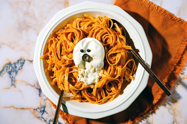 A bowl of fettuccine with smoky tomato sauce and a burrata ghost placed on an orange napkin.
