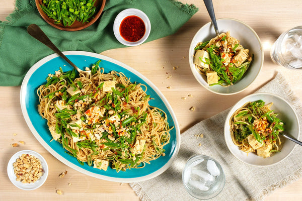Noodle dish with vegetables and tofu on a blue platter, surrounded by smaller servings and condiments.