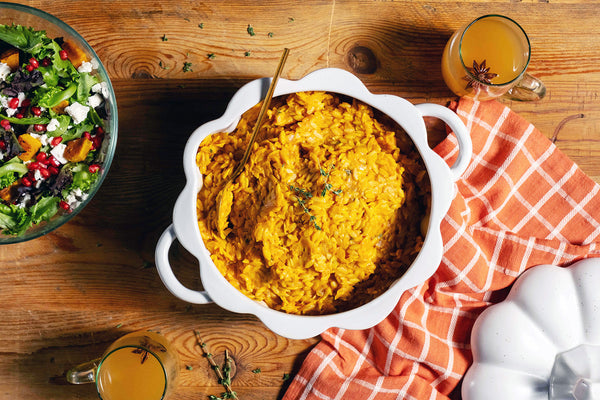 A bowl of pumpkin orzotto next to a greens salad and orange dish towel.