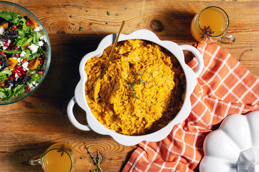 A bowl of pumpkin orzotto next to a greens salad and orange dish towel.