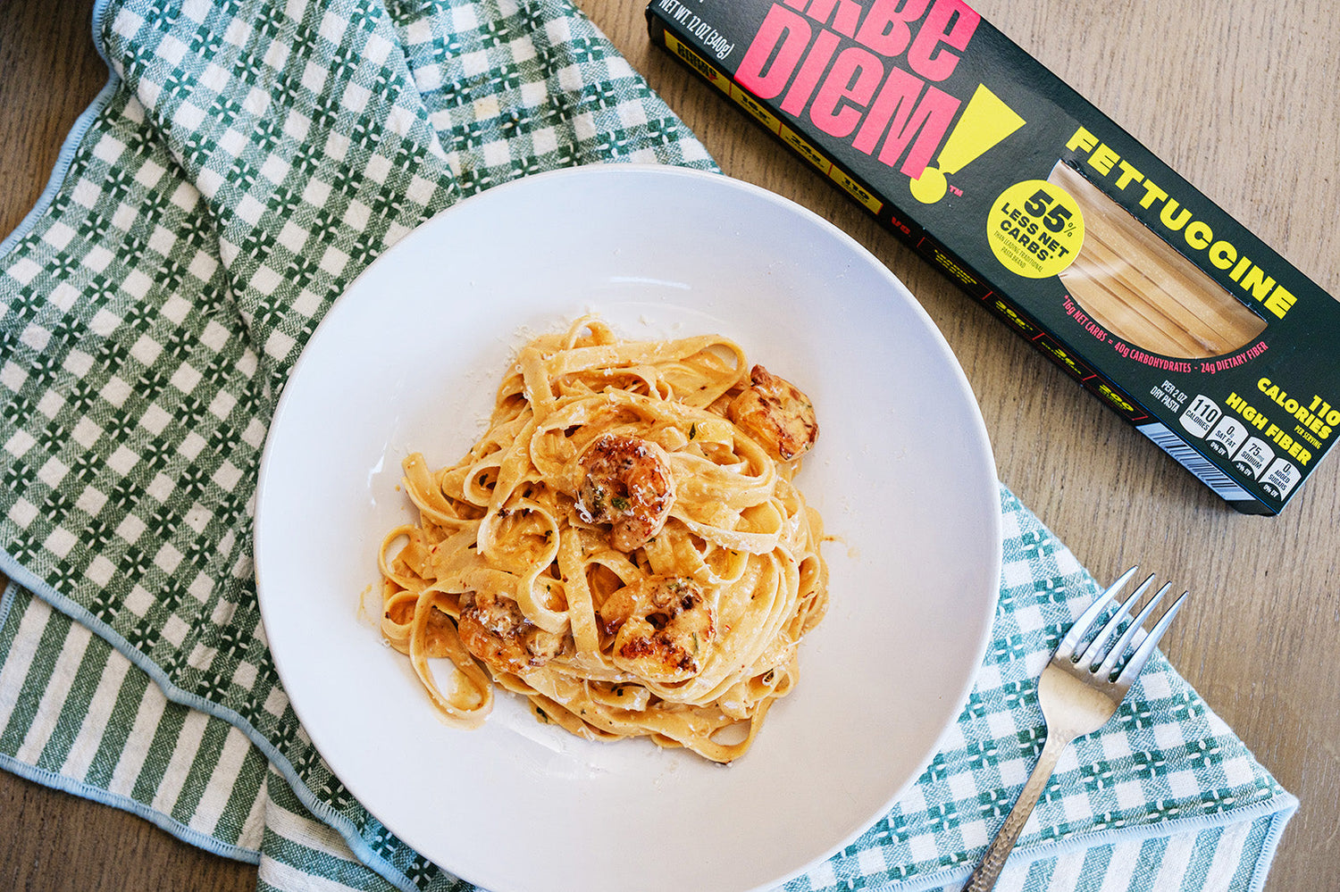 Plate of pasta with a box of Fettuccine noodles on a checkered cloth.