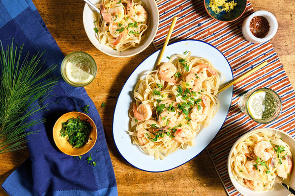A plate of shrimp scampi and noodles on a striped tablerunner