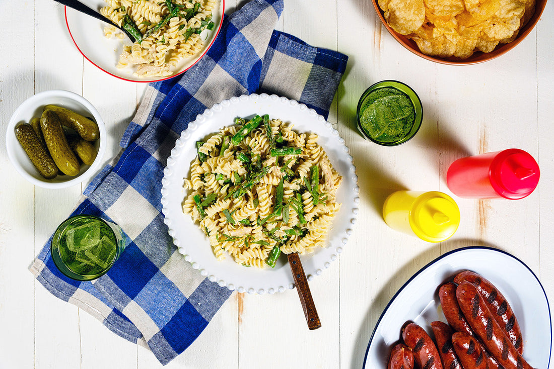 Assorted food items including pasta, pickles, and hot dogs on a checkered tablecloth.