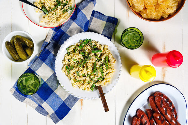 Assorted food items including pasta, pickles, and hot dogs on a checkered tablecloth.