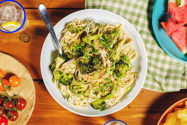 Plate of spaghetti with broccoli on a wooden table with a glass of water and watermelon.