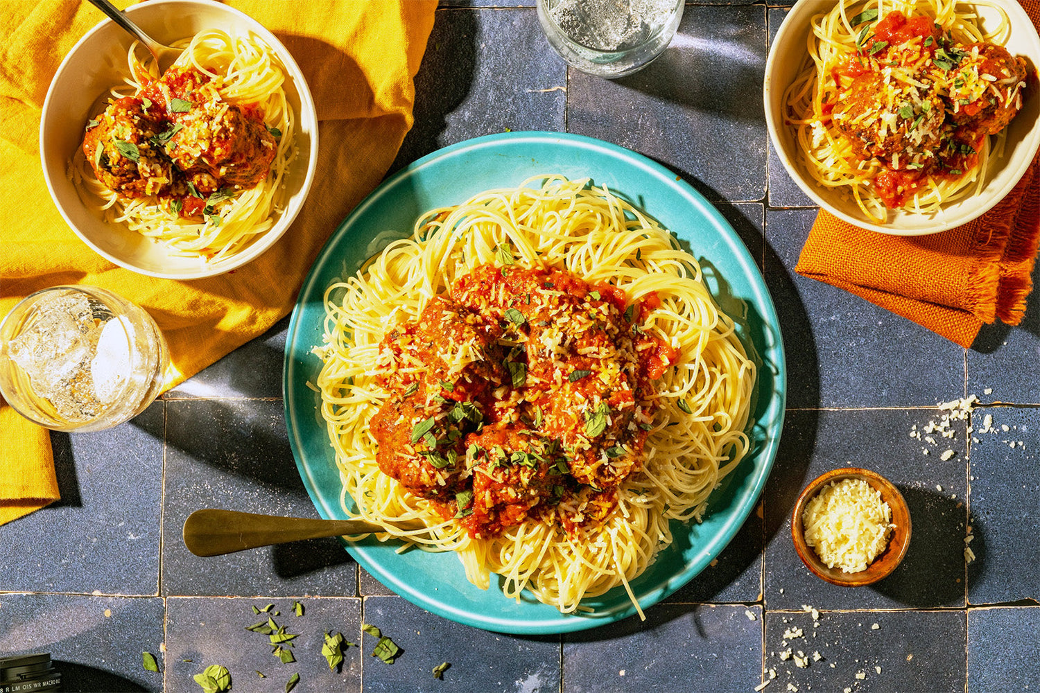 Plates of spaghetti with tomato sauce on a blue tiled table.