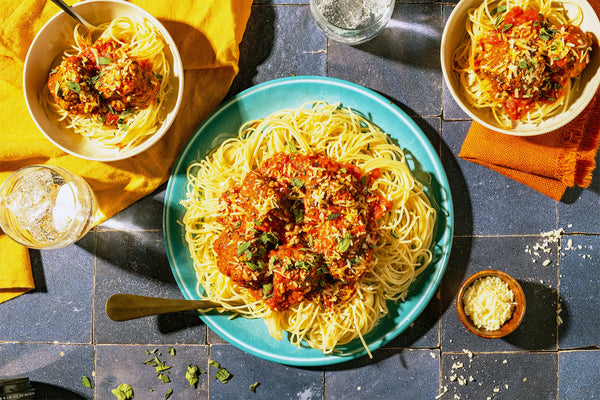 Plates of spaghetti with tomato sauce on a blue tiled table.