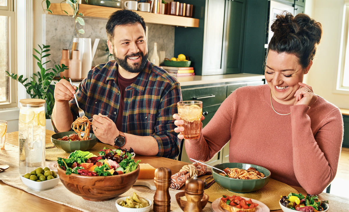 Man and woman enjoying a meal together at a kitchen table with various dishes and drinks.