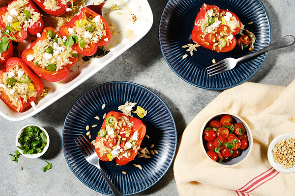 Two plates with Orzo Stuffed Red Peppers next to a casserole dish.
