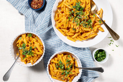 Three bowls of penne pasta with a creamy red sauce on a light surface with a blue cloth.