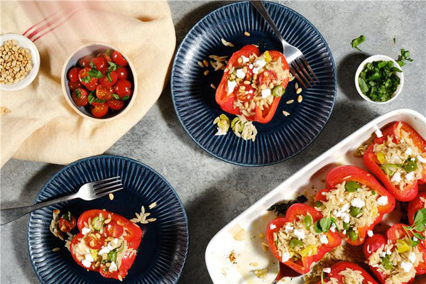 Stuffed bell peppers on plates with a bowl of cherry tomatoes and a dish of nuts.
