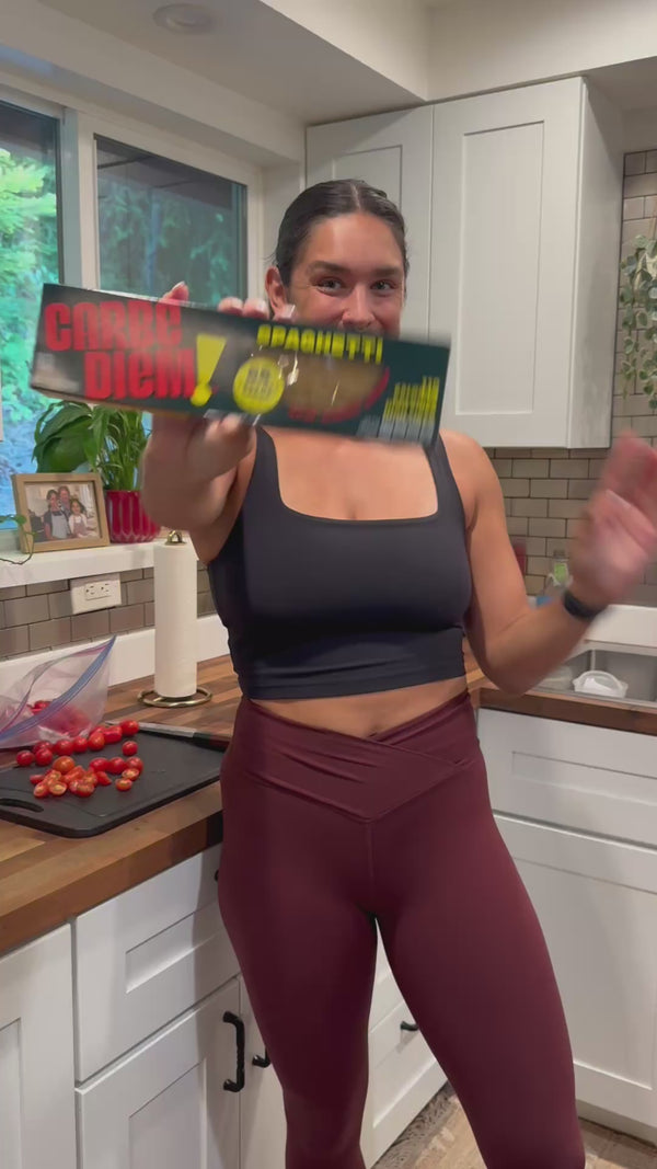 Load video: A woman in work out clothes holding a box of Carbe Diem spaghetti 