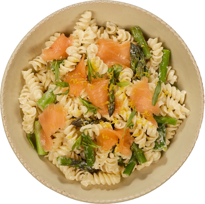 Pasta dish with salmon and green vegetables in a beige bowl
